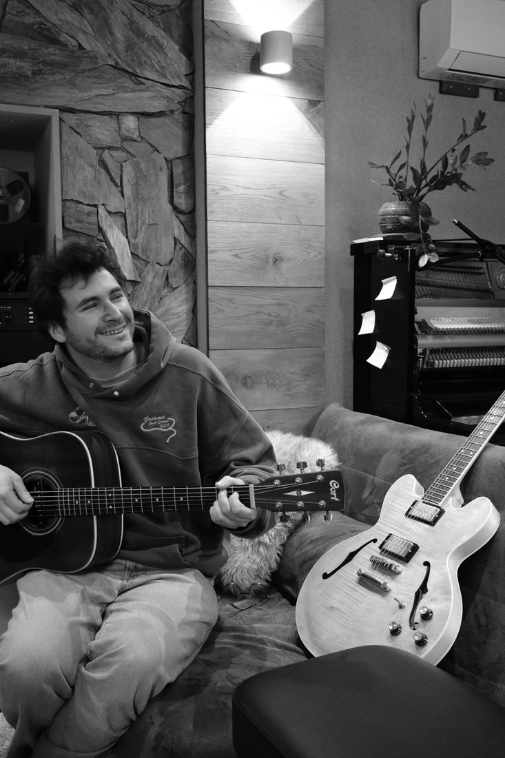Côme joue de la guitare sur un canapé de studio