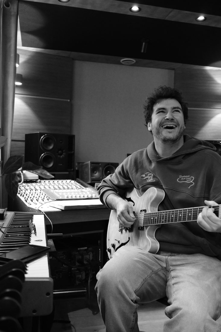 Côme éclate de rire en studio, guitare électrique en main